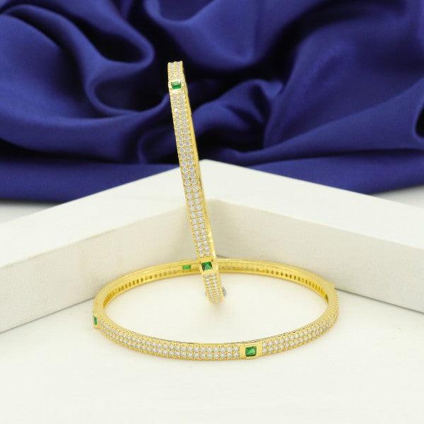 Elegant gold bangles with emerald accents and intricate detailing on a blue satin background.