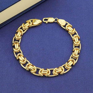 Gold bracelet with intricate chain design on blue cloth background.