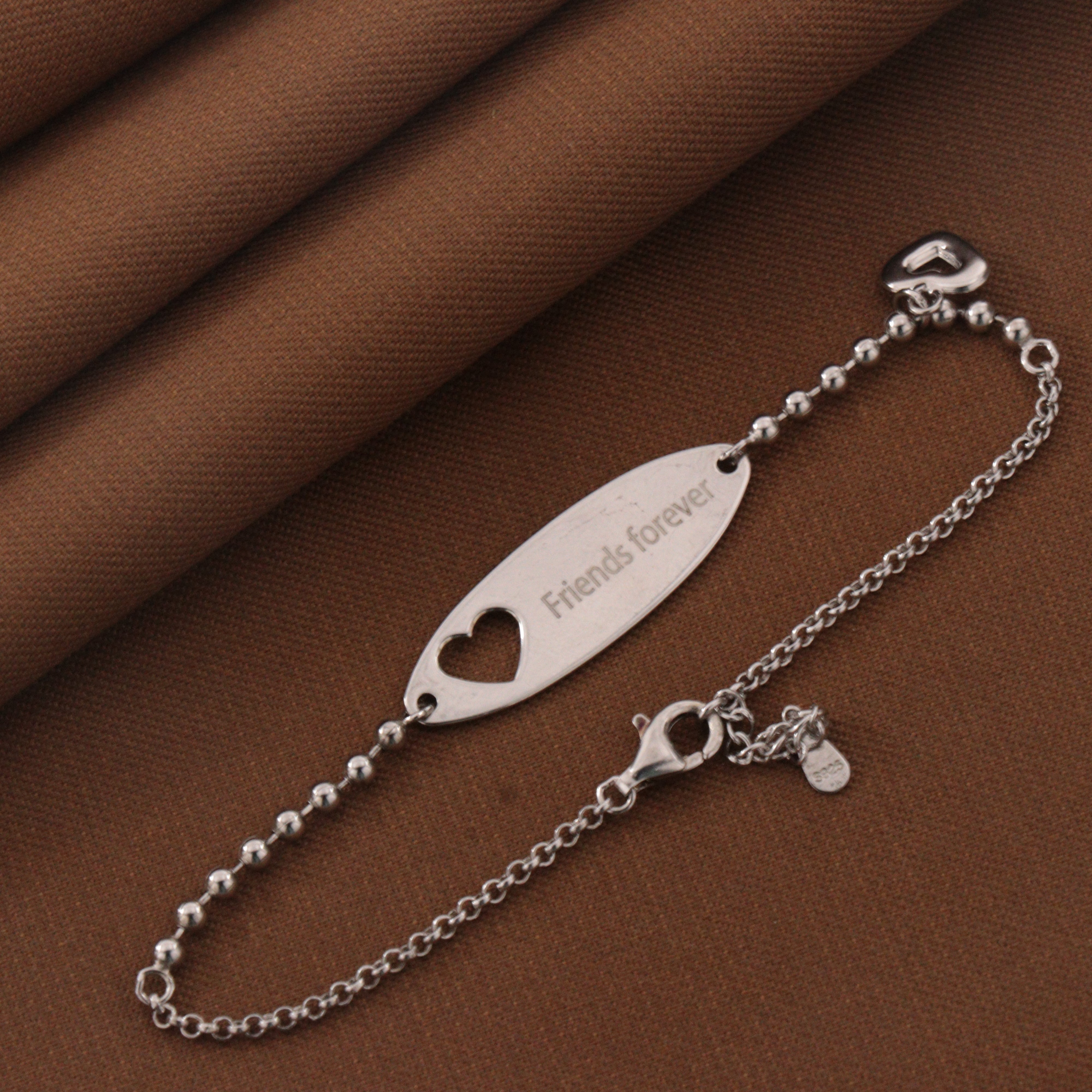 925 silver bracelet with "Friends forever" engraving and heart design on a brown fabric background.