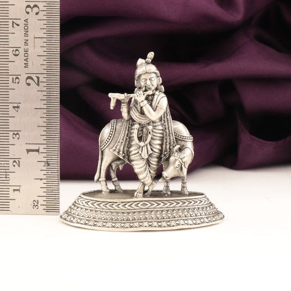 925 silver Krishna idol with cow, 43g and 6cms in height, showcasing intricate design and purity, placed next to a measurement scale.