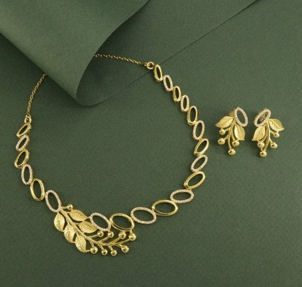 Elegant gold leaf design necklace with matching earrings on green background.