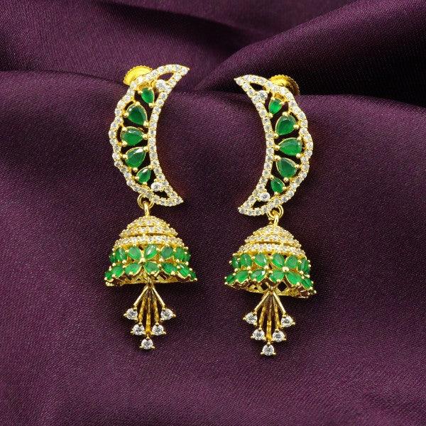 Intricately designed gold and green traditional Jhumka earrings with crescent moon motifs on a dark purple fabric backdrop.