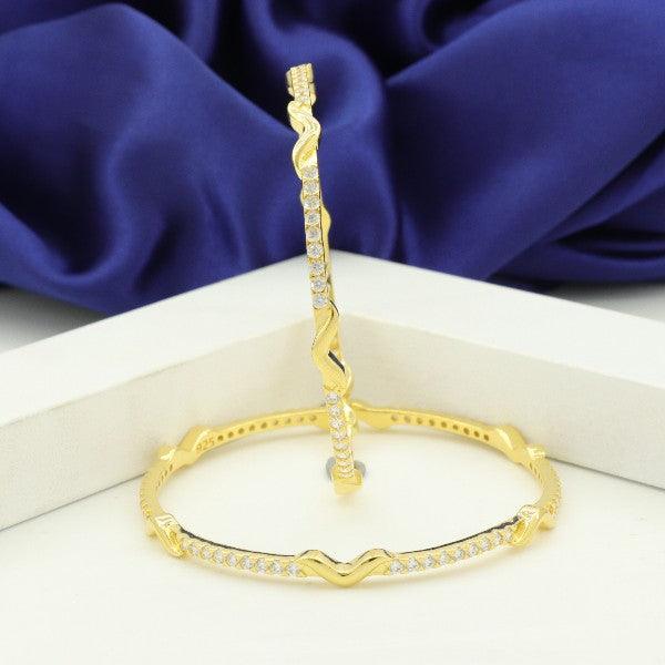 Elegant gold bangles with diamond embellishments on a white and purple fabric background.