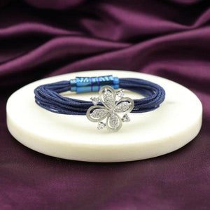 Elegant bracelet with a silver flower charm on blue threads, displayed on a white round platform against a deep purple fabric background.