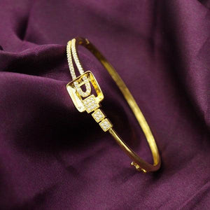 Elegant gold-plated bangle with square buckle design on a purple fabric background