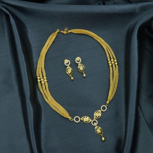 Gold necklace and earrings set displayed on dark fabric