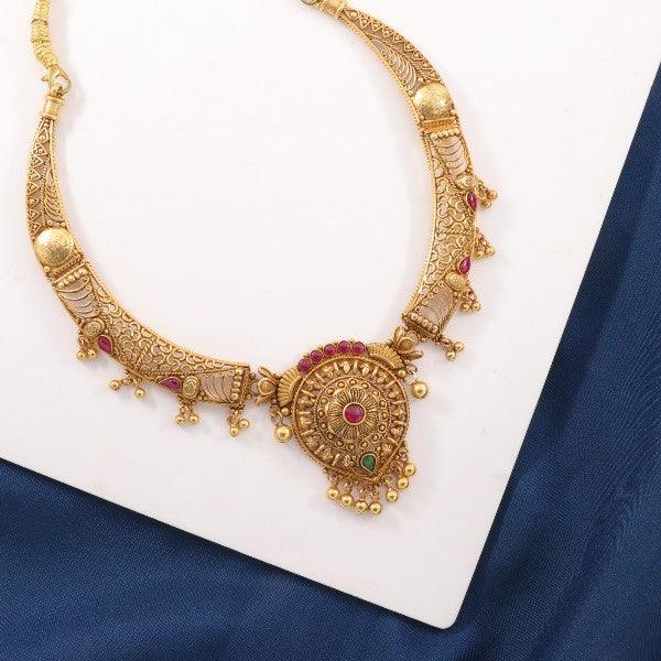 Intricately designed gold necklace with decorative red and green gemstones displayed on a white and blue background.