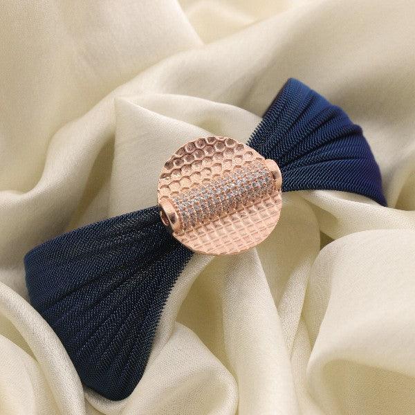 Elegant navy blue bow hair accessory with a textured rose gold centerpiece on a cream fabric background